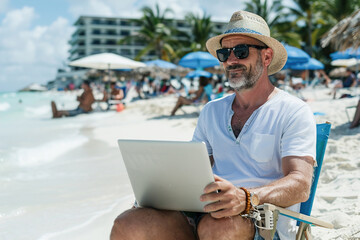 Cheerful businessman works on his laptop confidently while relaxing on a vibrant, sunlit beach