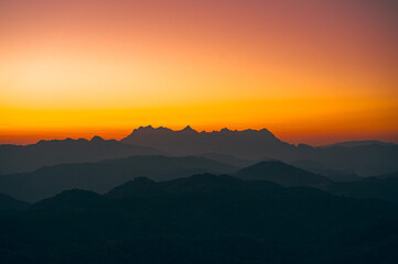 High-angle view of a beautiful orange, pink, and yellow sky in the evening as the sun sets. There is a view of Doi Luang Chiang Dao Mountain in the center of the image, which has a unique shape.