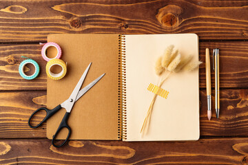 Crafting session with notebook, scissors, and decorative tape on a wooden table