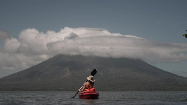A mature woman enjoys kayaking on Lake Ometepe, embracing the stunning view of Concepcion volcano. The vibrant atmosphere and landscape highlight her adventure in Nicaragua.