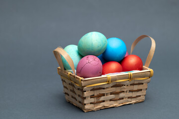 Colored  Easter eggs in small wooden basket on the gray background  ready for Easter