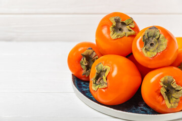 Persimmon on textured wooden background. Persimmon fruit. A piece of ripe, juicy, sweet persimmon fruit. Vegan. Orchard. Close-up. Space for text. Copy space.