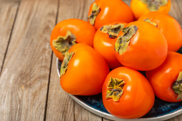 Persimmon on textured wooden background. Persimmon fruit. A piece of ripe, juicy, sweet persimmon fruit. Vegan. Orchard. Close-up. Space for text. Copy space.