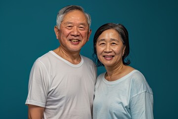 Fototapeta premium Portrait of a satisfied asian couple in their 60s dressed in a casual t-shirt while standing against solid color backdrop
