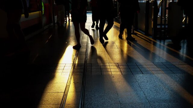 Silhouette of crowd people walking against sunset light. Shadows of busy pedestrians walking after work through a golden sunset on a train station. Long shadows and warm lights of evening atmosphere.