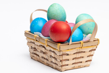 Colored homemade Easter eggs in small wooden basket isolated on the white background.