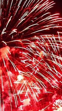 Red fireworks exploding in the night sky with trails of light. Vertical shot of celebration and festive concept
