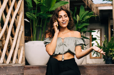 Positive woman speaking on smartphone sitting on steps of wooden veranda