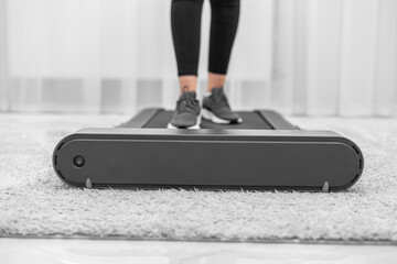 A person wearing black leggings and gray sneakers is walking on a compact treadmill in a modern, minimalistic home environment, focusing on fitness and an active lifestyle.