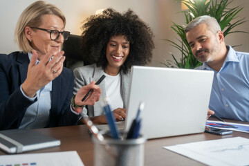 Three busy happy middle aged professional business man and two women executive leaders team using laptop working on computer at work desk having conversation on financial project at meeting in office.