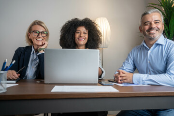 Sits by the table with laptops. Confident business people in formal clothes working in the office. Small group of smiling diverse businesspeople using a laptop together at work.	