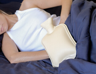 The girl lies in bed with a heating pad on her stomach, experiencing menstrual pain © Яна Нестеренко