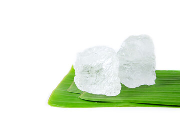 Pieces of white alum sit on a banana leaf, set against a white background. This simple yet...