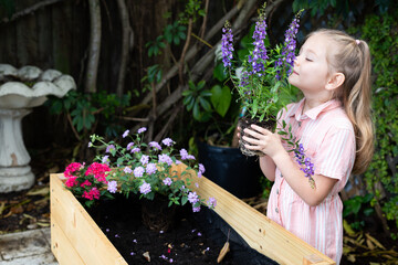 little Caucasian girl planting flowers into flower bed. Butterfly garden. Summer activities for kids. Kids and environment concept