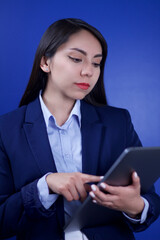 Mujer corporativa concentrada sosteniendo tableta digital con fondo azul 