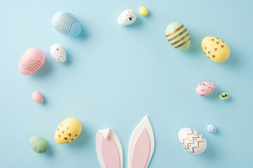 Colorful pastel Easter eggs arranged around pink bunny ears on a soft blue backdrop