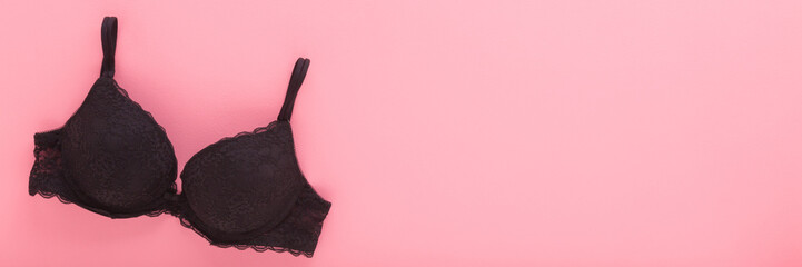 New dark black lace bra on light pink table background. Pastel color. Female casual underwear....