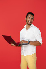 Smiling african american young man holding laptop over red background.