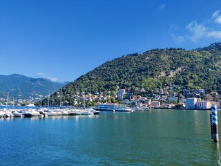 Commo, Italy - 9 June 2023: Summertime at Bellagio lakeside, lake of Como. Beautiful Italian Commune, Bellagio with alps mountains, old architecture buildings, and clear sky. Boat dock landscape. 