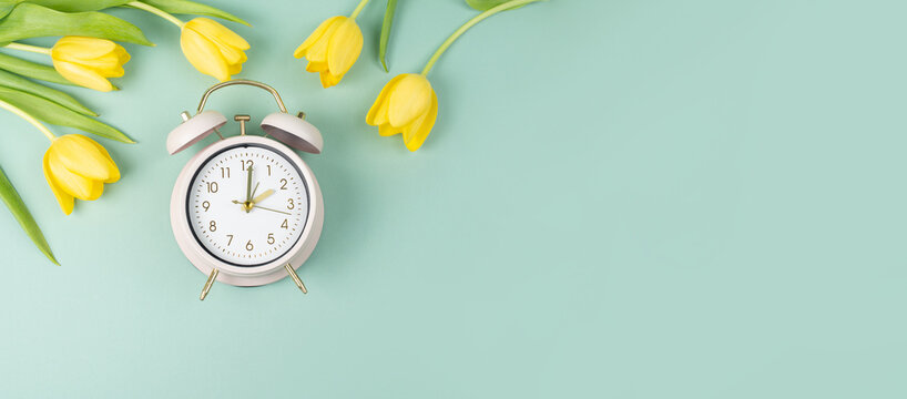 Alarm clock with yellow tulip flowers, switch to daylight saving time in spring, summer time changeover