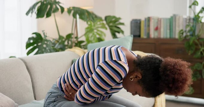 Sick, home and woman with period cramps, pain or stomach ache with medical emergency on sofa. Diarrhea, constipation and African person with problem, digestion or gut health with appendicitis disease