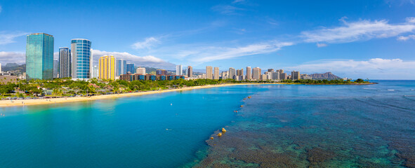 Aerial view of Waikiki Beach in Honolulu, Hawaii, with turquoise waters, coral reefs, high rise buildings, and Diamond Head crater in the background. © Aerial Film Studio