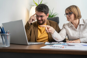 Two smiling diverse businesspeople using a laptop together at the office.