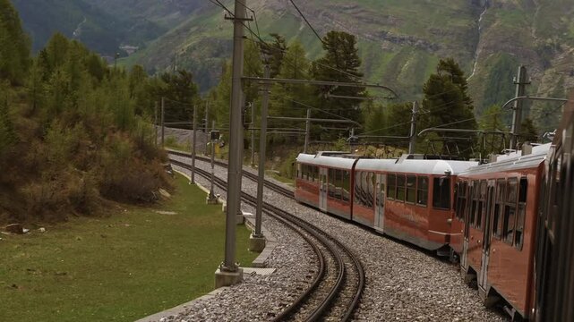 POV from a red train passing through a scenic mountain landscape. The Gornergrat train runs downhill toward Zermatt, offering stunning Alpine views. Perfect for travel and adventure themes