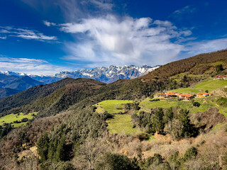 A charming rural village with red-tiled roofs nestled in lush green hills, set against the majestic...
