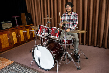 Young drummer playing a red drum set in a cozy music room