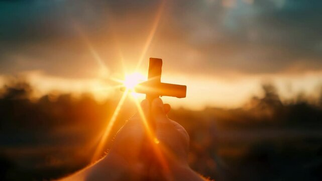 Devout believer in god holding a Cristian cross at sunset with sun shining through it