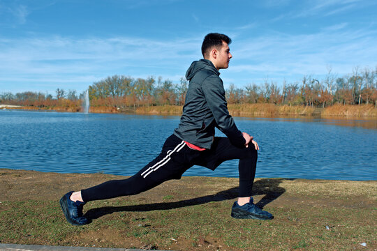 Man Stretching Outdoors by Lake on a Calm Day in Athletic Wear