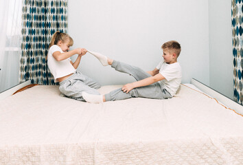 A little girl takes her brother's sock off and lightly tickles him. children laugh.
