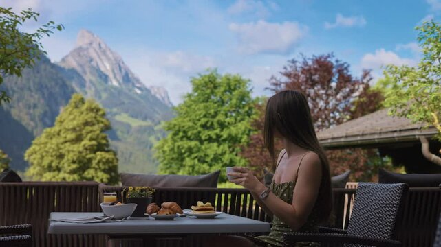 Tourist beautiful woman drinking coffee at breakfast on a terrace with a stunning view of the Alps at sunrise. Perfect for lifestyle and vacation concepts in Switzerland  