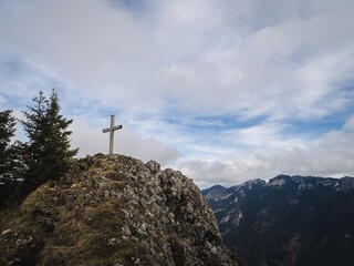 A hiker with a backpack walks along a moss-covered trail surrounded by tall pine trees. The rugged terrain and tranquil forest create a peaceful outdoor adventure scene.