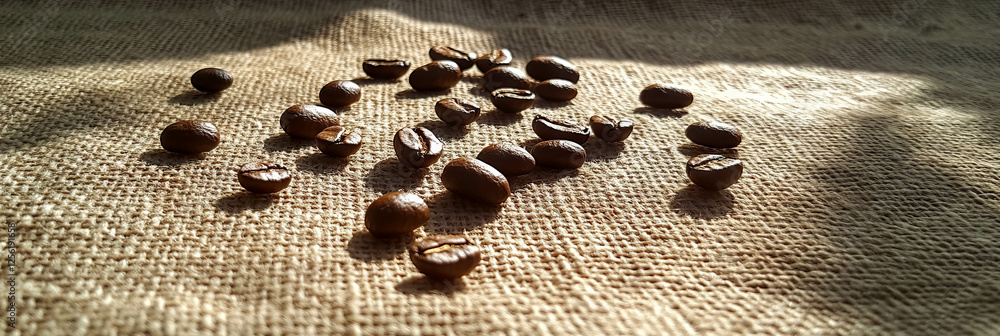 Aufkleber scattered coffee beans creating a textured display on burlap in bright lighting