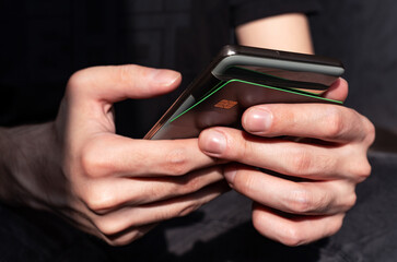 Close-up of male hands applying a bank credit card to the back cover of a smartphone for data reading, online payment and expense tracking, NFC.