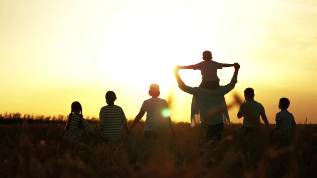 Silhouettes of huge happy family at golden sunset in field. Peaceful calm family children kids parents holding hands, walking across field in setting sun. Mom dad kids sisters brothers stroll together