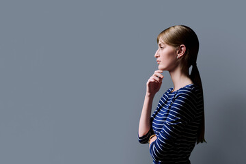 Fototapeta premium Profile view, young serious female looking forward on gray studio background
