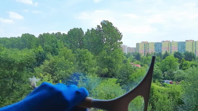 Female hand in a cleaning glove using a squeegee to wash a window at home, close-up shot of a woman’s hand Washing windows without streaks holds Glass wiper. House cleaning and cleanliness