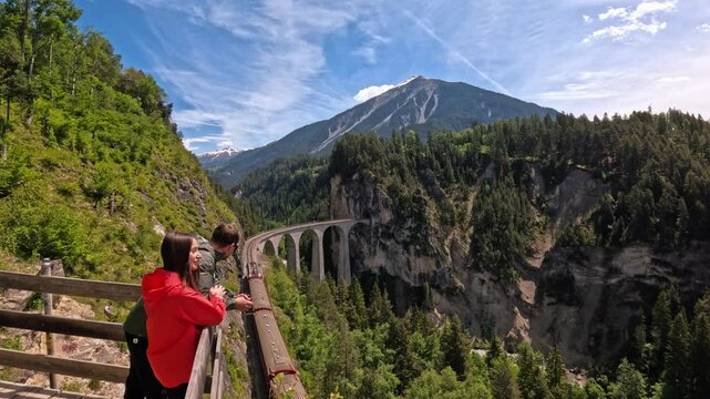 Lifestyle video of a tourist couple watching the train passing on Landwasser Viaduct on a beautiful sunny day. Perfect for lifestyle, travel, vacation, and adventure in the Swiss Alps
