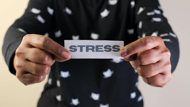 A person displays a paper with the word stress printed on it, highlighting mental health awareness and emotions.