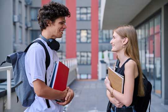 Young friends students teenage guy and girl talking together, urban background