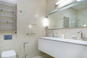 Modern bathroom design decorated with light beige tiles. White furniture, illuminated mirror and stylish accessories.