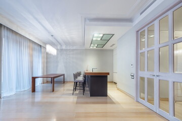 The kitchen area in the apartment is decorated in white. Double-leaf door with glass windows. Stylish ceiling lamp above the dining table.