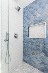 A shower detail with blue scale tiles and white subway tile walls, chrome faucet, and white stone...