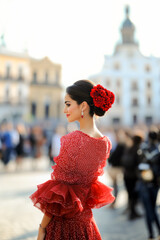Flamenco dancer wearing a traditional red dress with flower in her hair, posing in a seville square, andalusia, spain