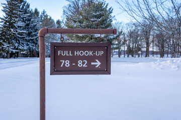 Winter, snow covered brown wooden sign Full Hook Up in a park campground.