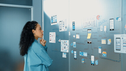 Professional young beautiful businesswoman thinking while standing at glass board with colorful...