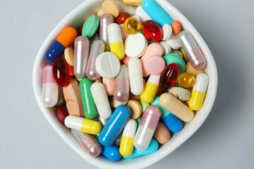 Various pills in a bowl on gray background